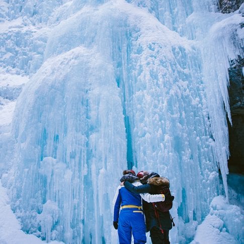 two girls hugging in front of frozen waterfall